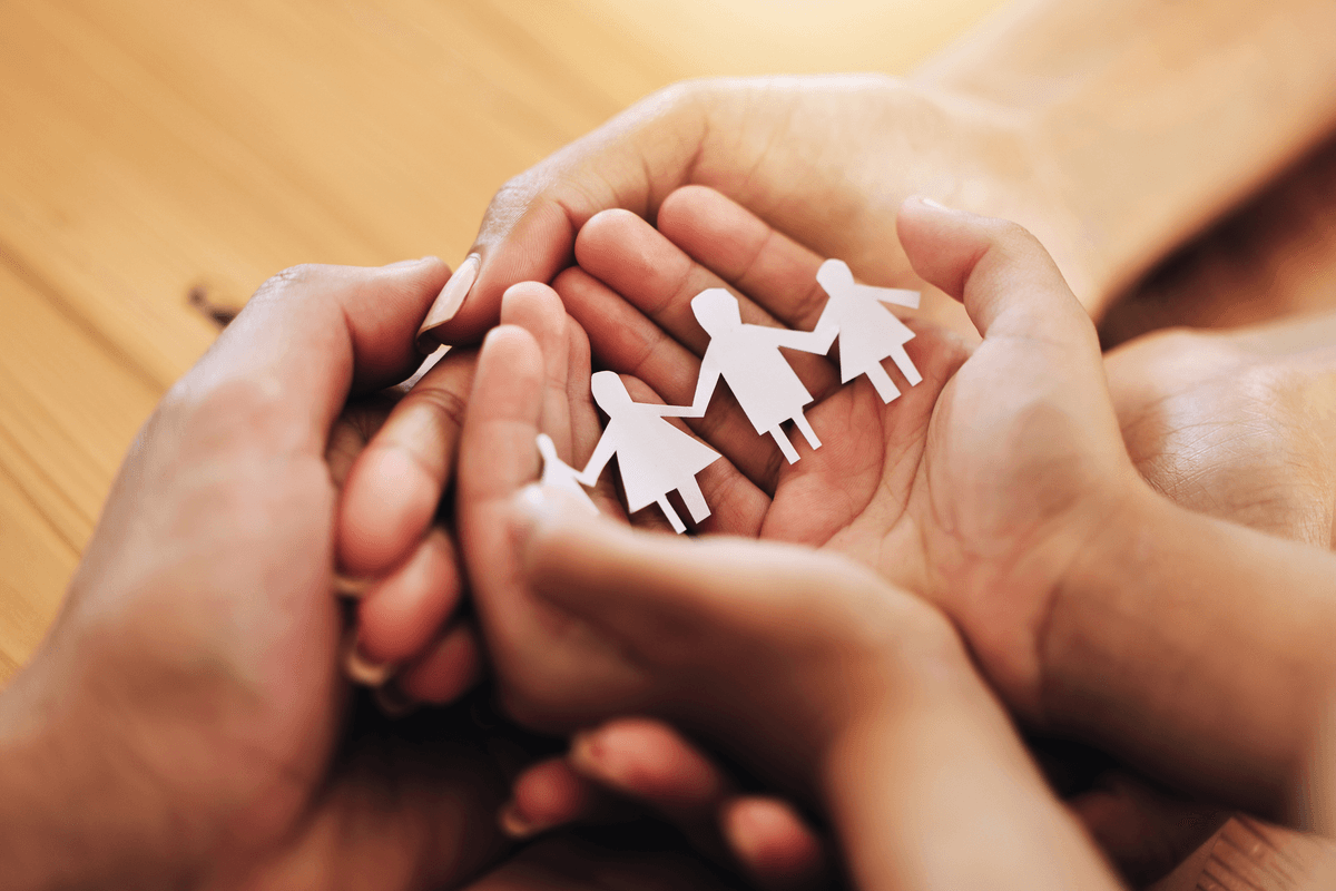 Hands cradling paper cutout family symbolizing foster care protection
